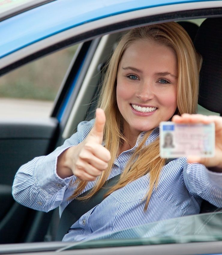 Junges Mädchen ist im Auto, hält ihren Führerschein in der Hand und macht einen Daumen nach oben